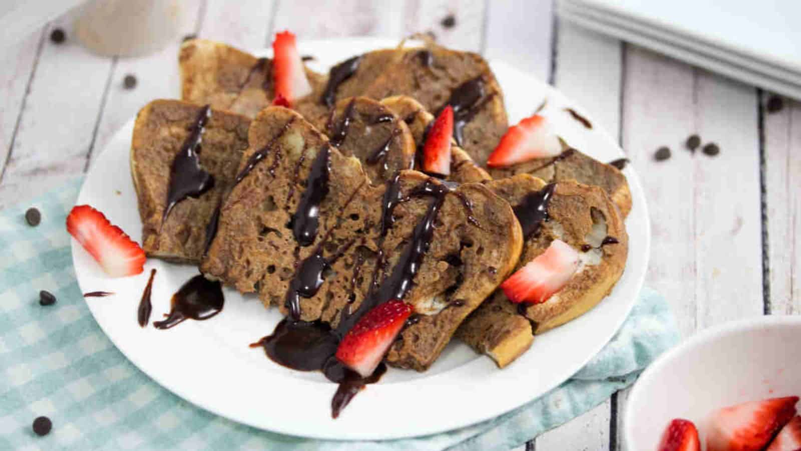 Chocolate protein French toast on a white plate drizzled with chocolate and strawberries with the plate on a blue linen.