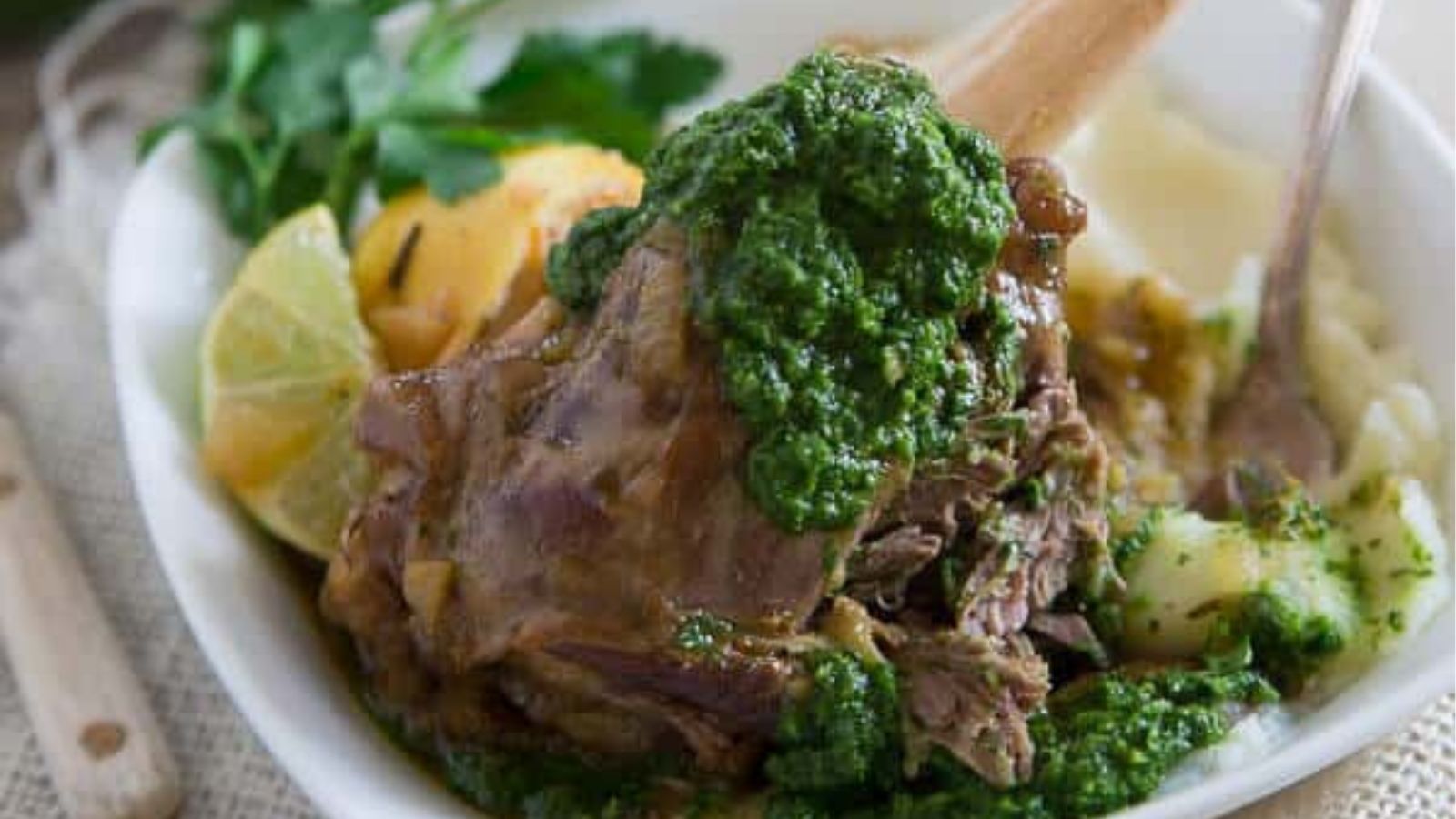 Close-up image of citrus based lamb shanks with green harissa on a plate.