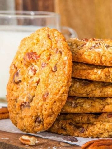 A close up image of a stack of cowboy cookies arranged on a serving platter with a glass of milk at the back.