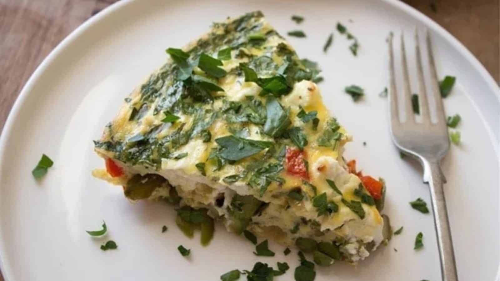 A slice of crustless quiche with vegetables and goat cheese on a white plate.