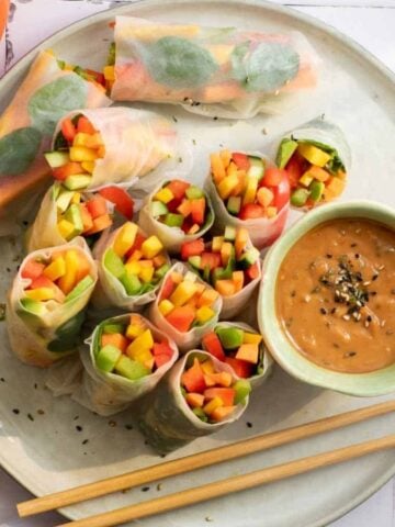Top view of Easy Rainbow Veggie Rolls on a plate with a dip and a pair of chopsticks.