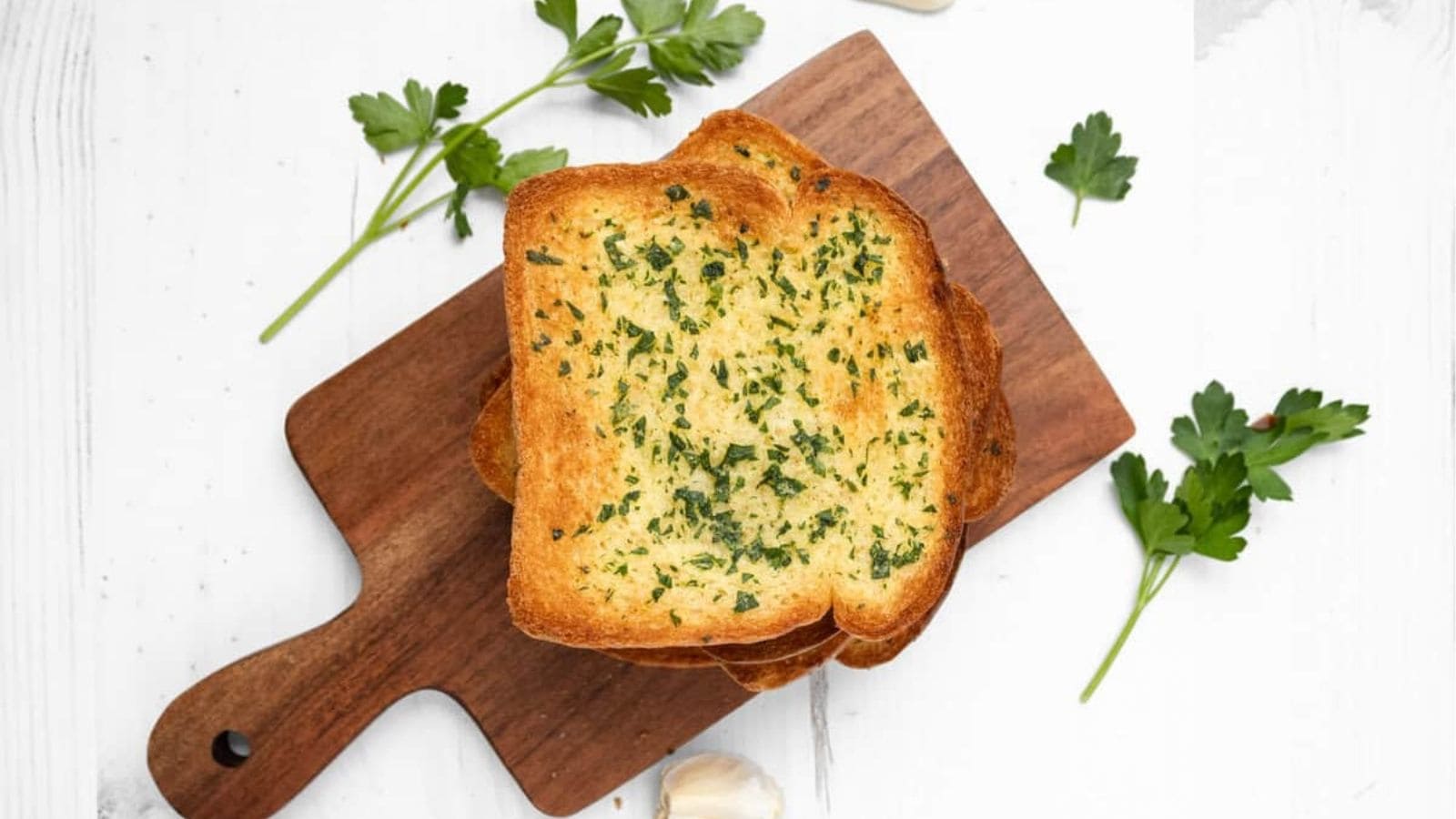 An overhead image of a piece of garlic bread on a wooden serving board.