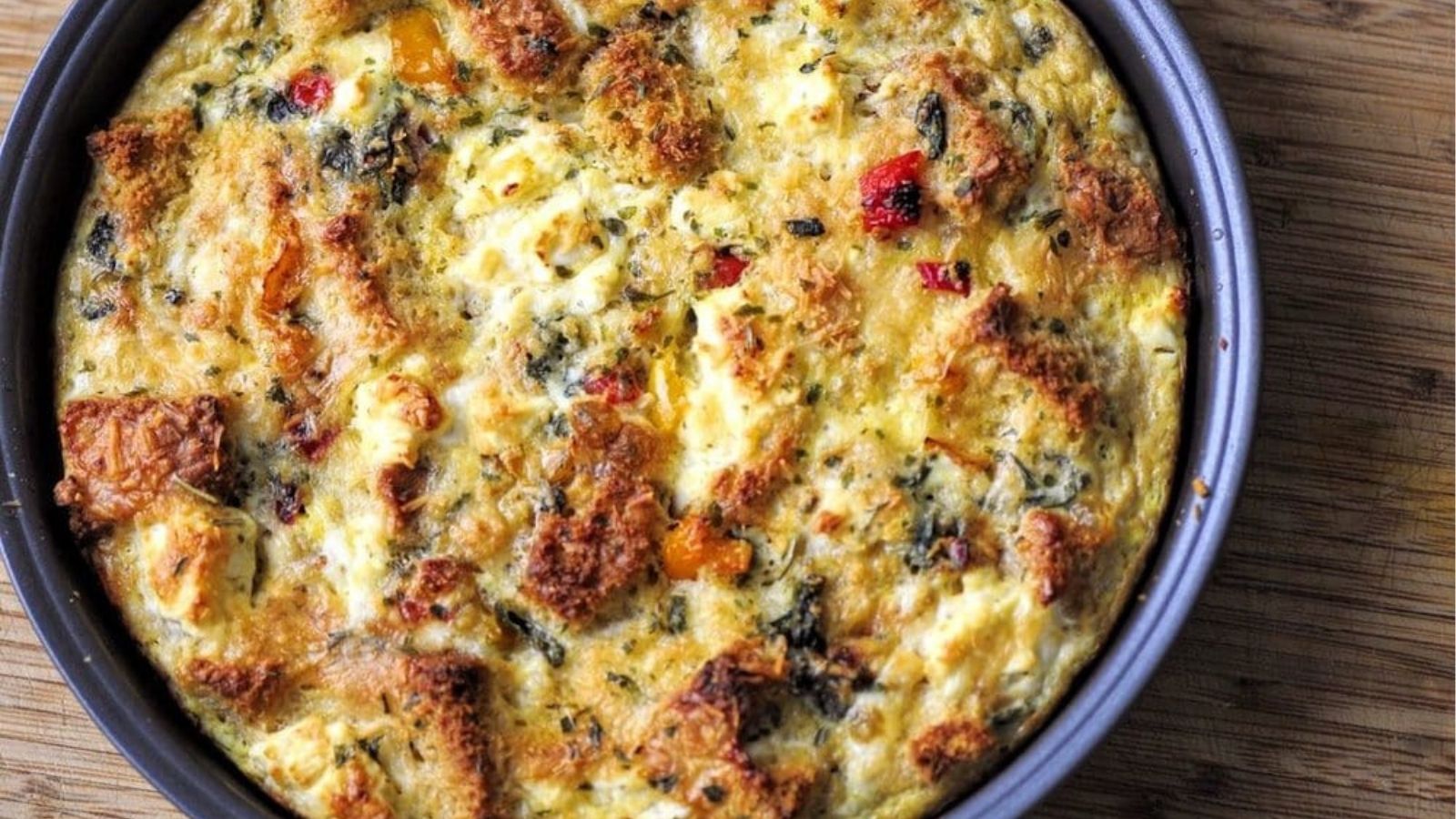 Overhead image of gluten free strata with cheese, spinach, and bell peppers in a skillet.