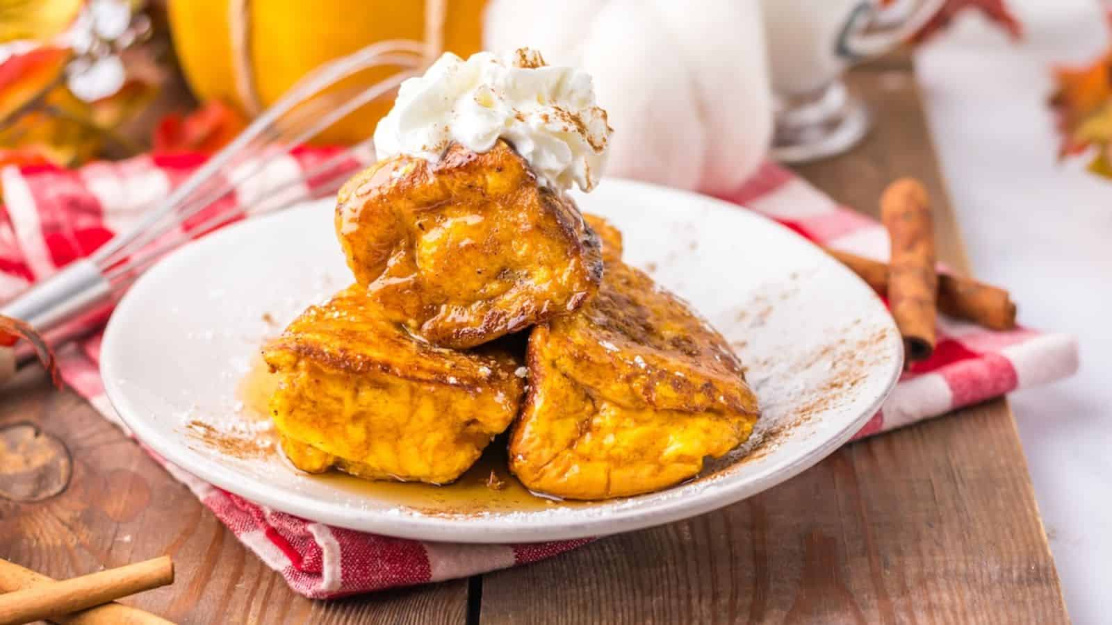 Three slices of Hawaiian Roll Pumpkin French toast topped with whipped cream and syrup on a white plate.