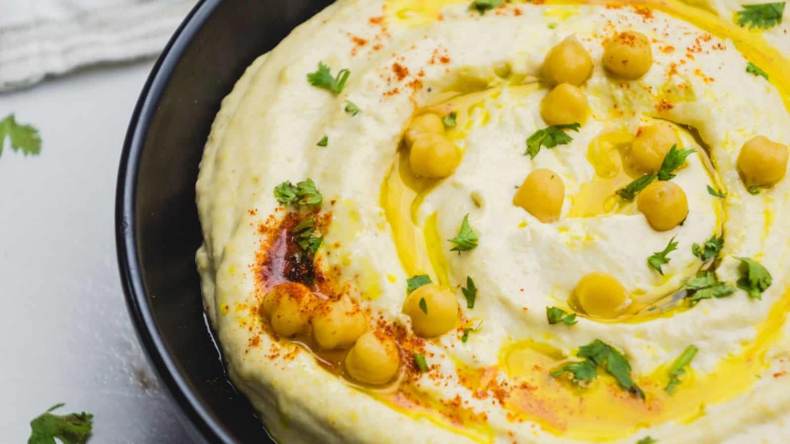 A bowl of hummus garnished with whole chickpeas, olive oil, and chopped herbs.