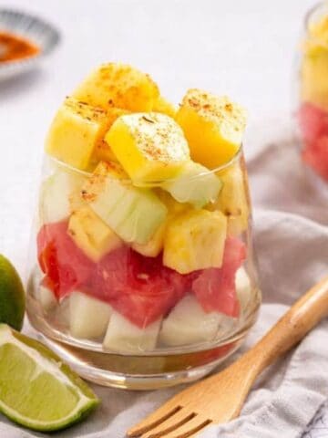 An image of Mexican fruit cup with sliced limes on the side.