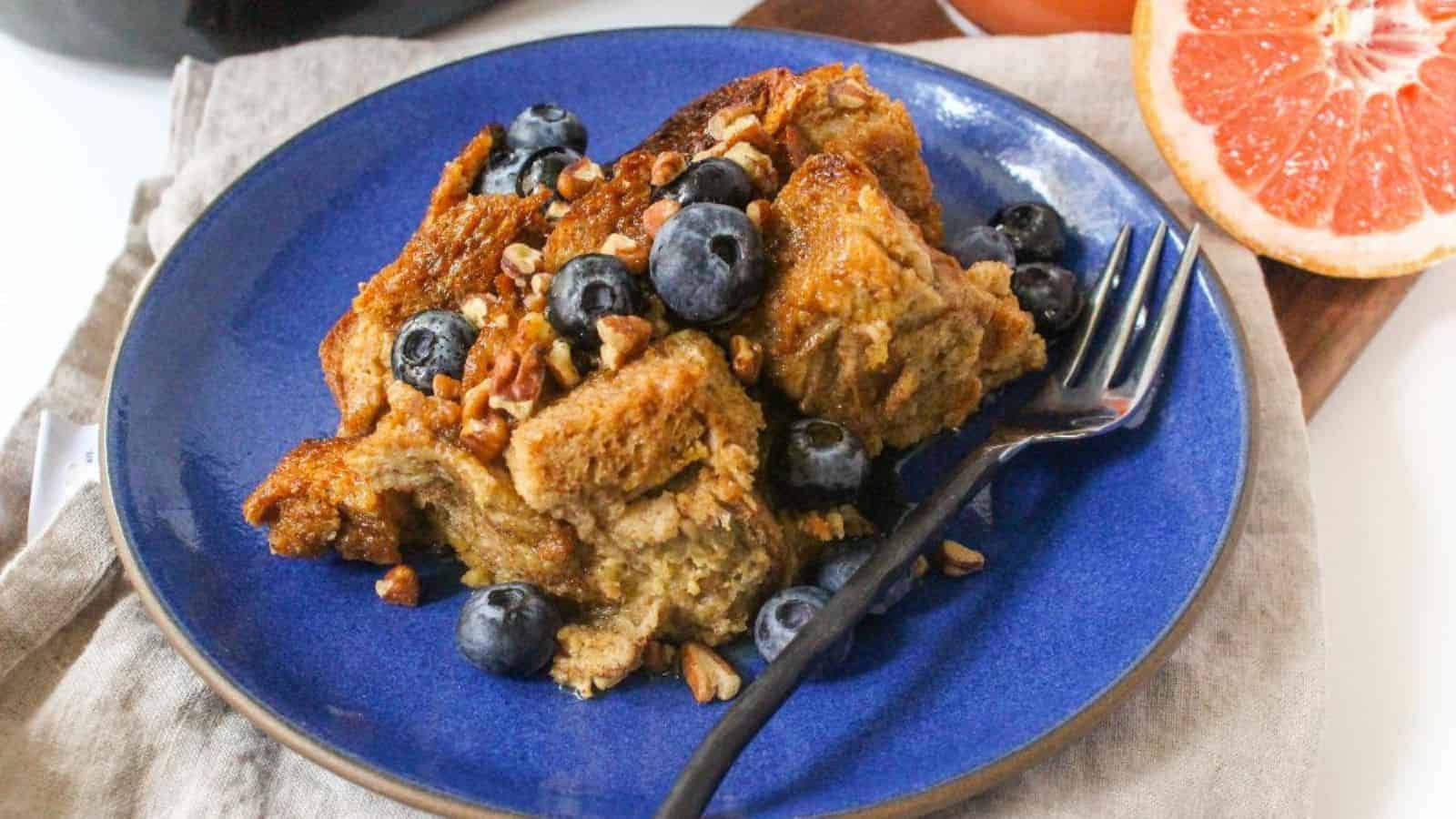 A slice of french toast casserole topped with blueberries and pecans on a blue plate.