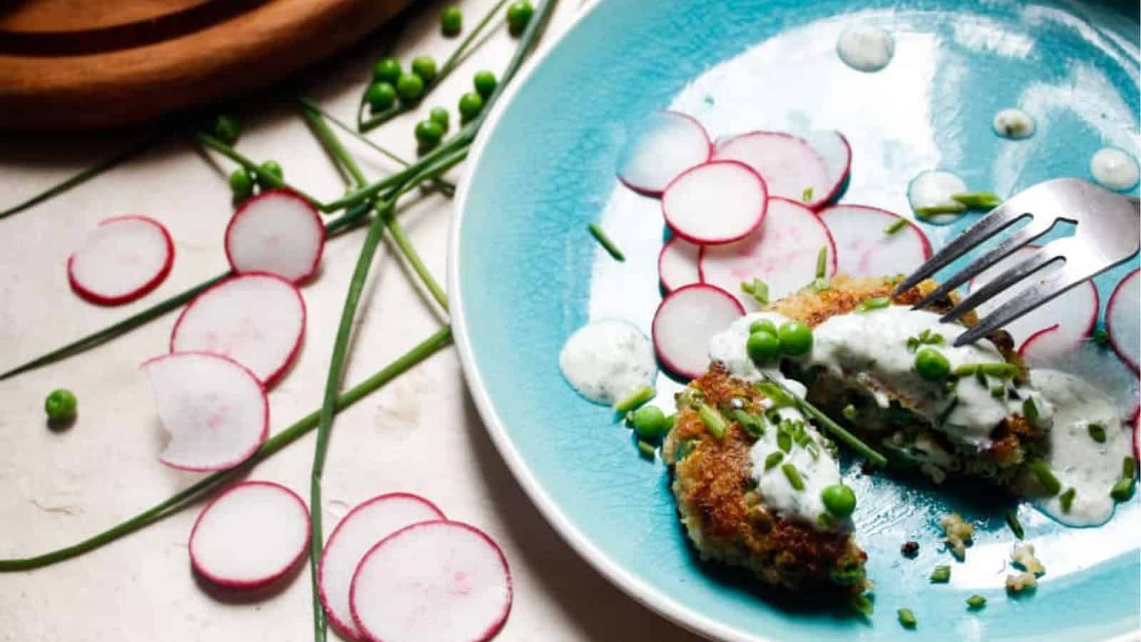 A sliced quinoa fritter with spring peas, feta, and cilantro chive yogurt sauce on a plate.