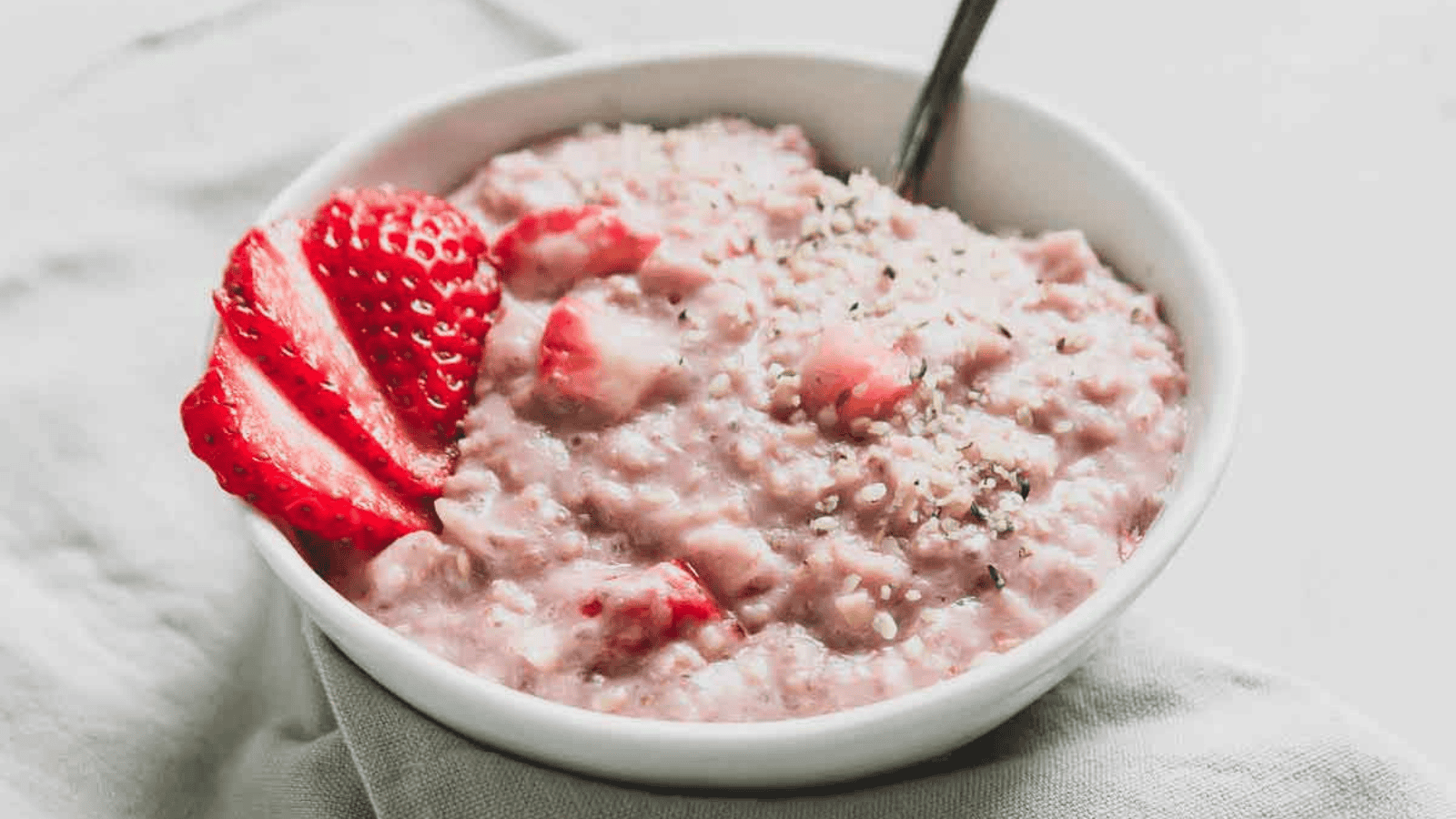Strawberries and cream oatmeal garnished with fresh strawberry slices in a bowl with a spoon.