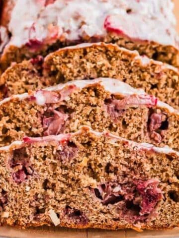 Slices of Strawberry Bread on a wooden board with fresh strawberries.