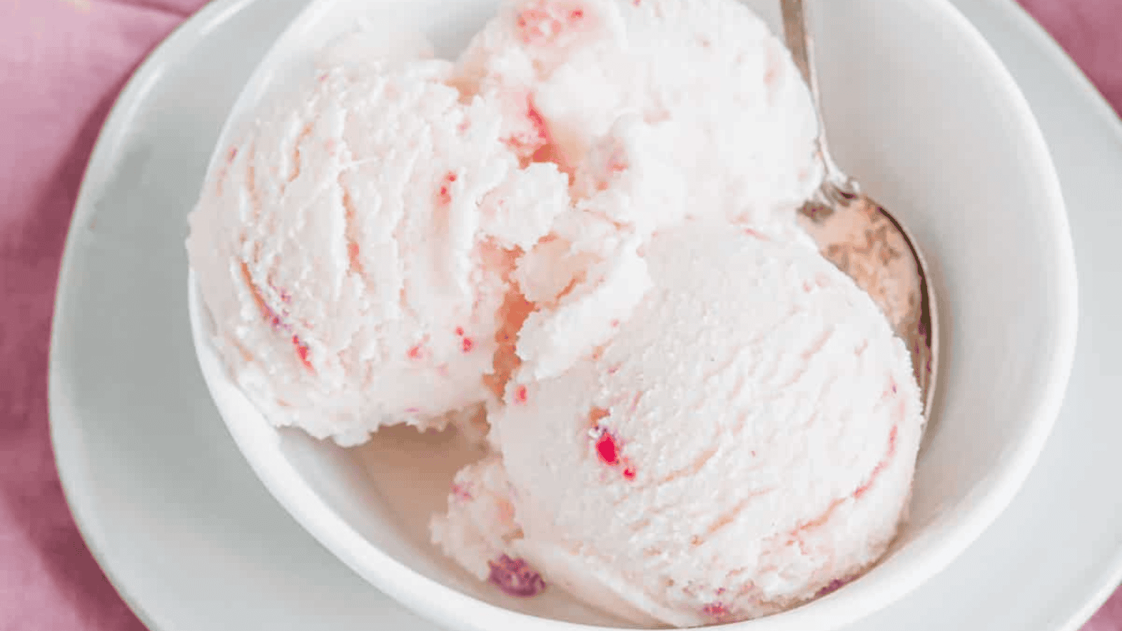Strawberry kefir ice cream in a white bowl with a silver spoon.