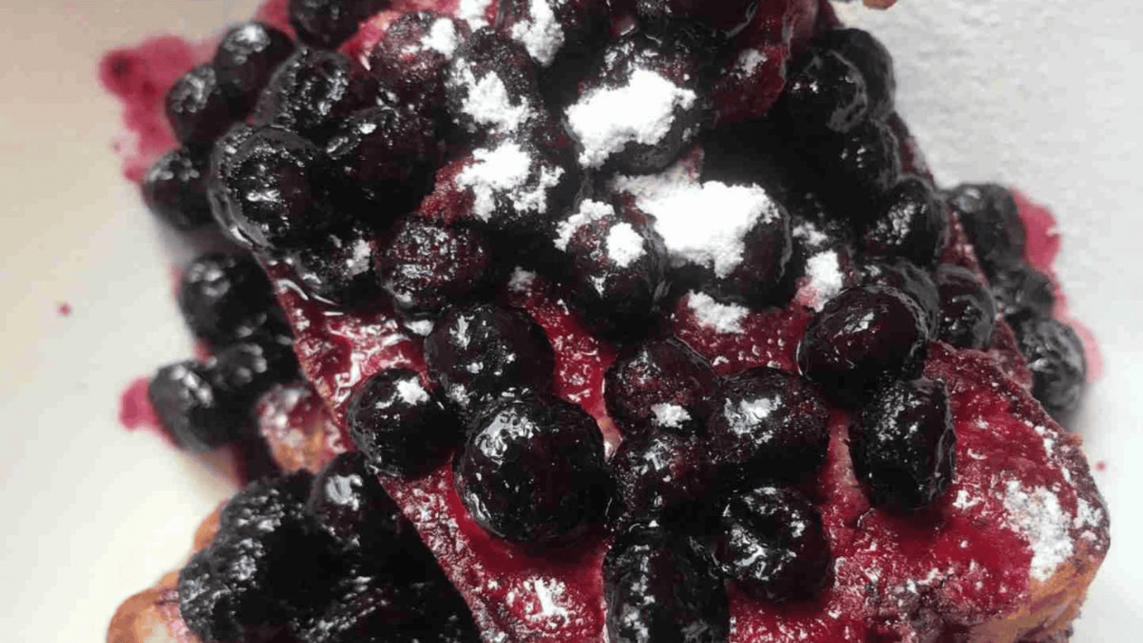 Waffles topped with a generous amount of blueberries and a dusting of powdered sugar.