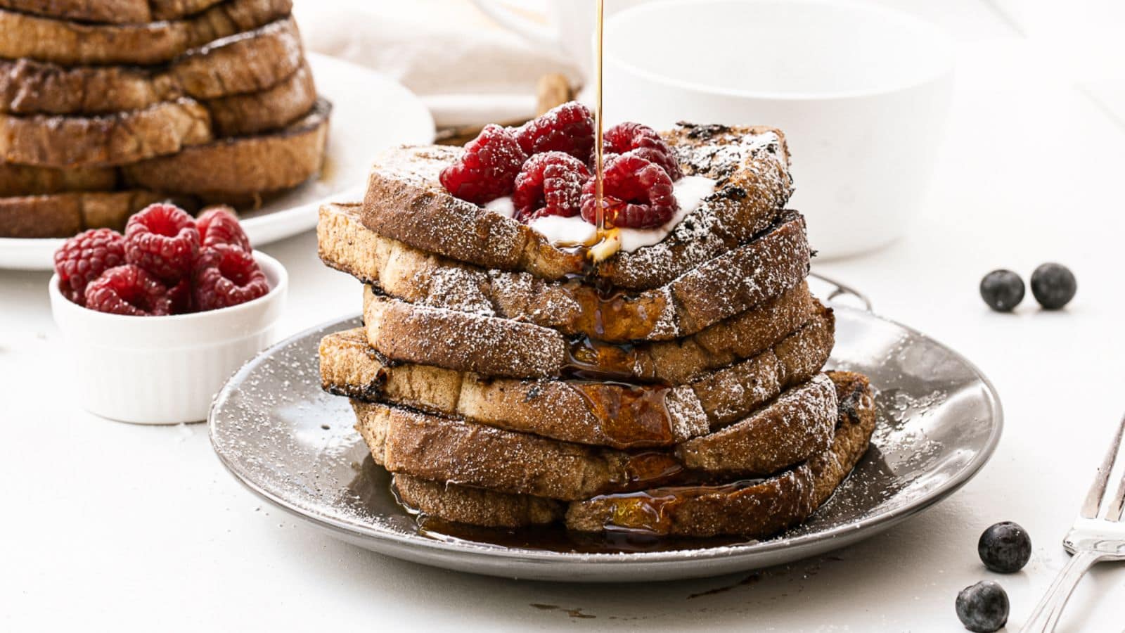Someone pouring syrup on a stack of Vegan French Toast on a plate.