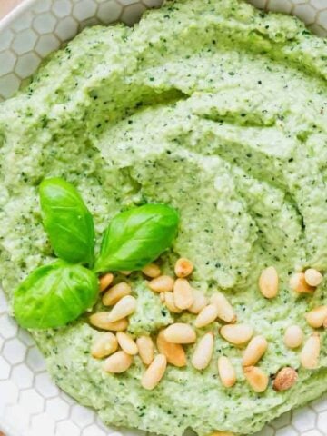 A close-up image of a bowl of Zucchini Pesto on a wooden board.