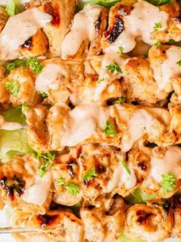 A plate with lettuce and five Bang Bang Chicken Skewers.