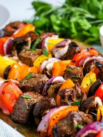 A closeup photo of a row of grilled steak kabobs.