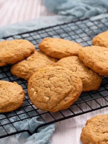 A closeup of pumpkin white chocolate chip cookies on a tray with a glass of milk.