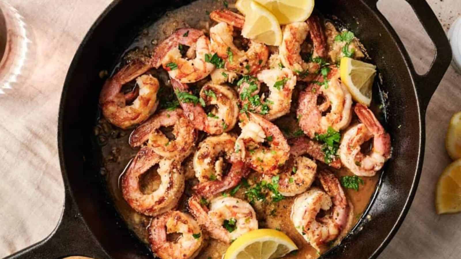An overhead shot of shrimp scampi with lemons and garnished with herbs in a skillet.