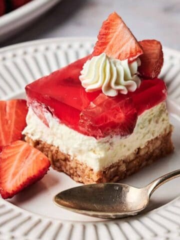 A slice of Strawberry Pretzel Salad on a plate with a spoon and some slices of fresh strawberries.