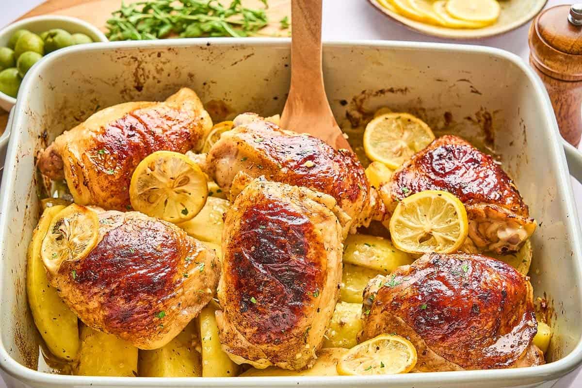Six chickens in a pan with lemons, garlic, and potatoes.
