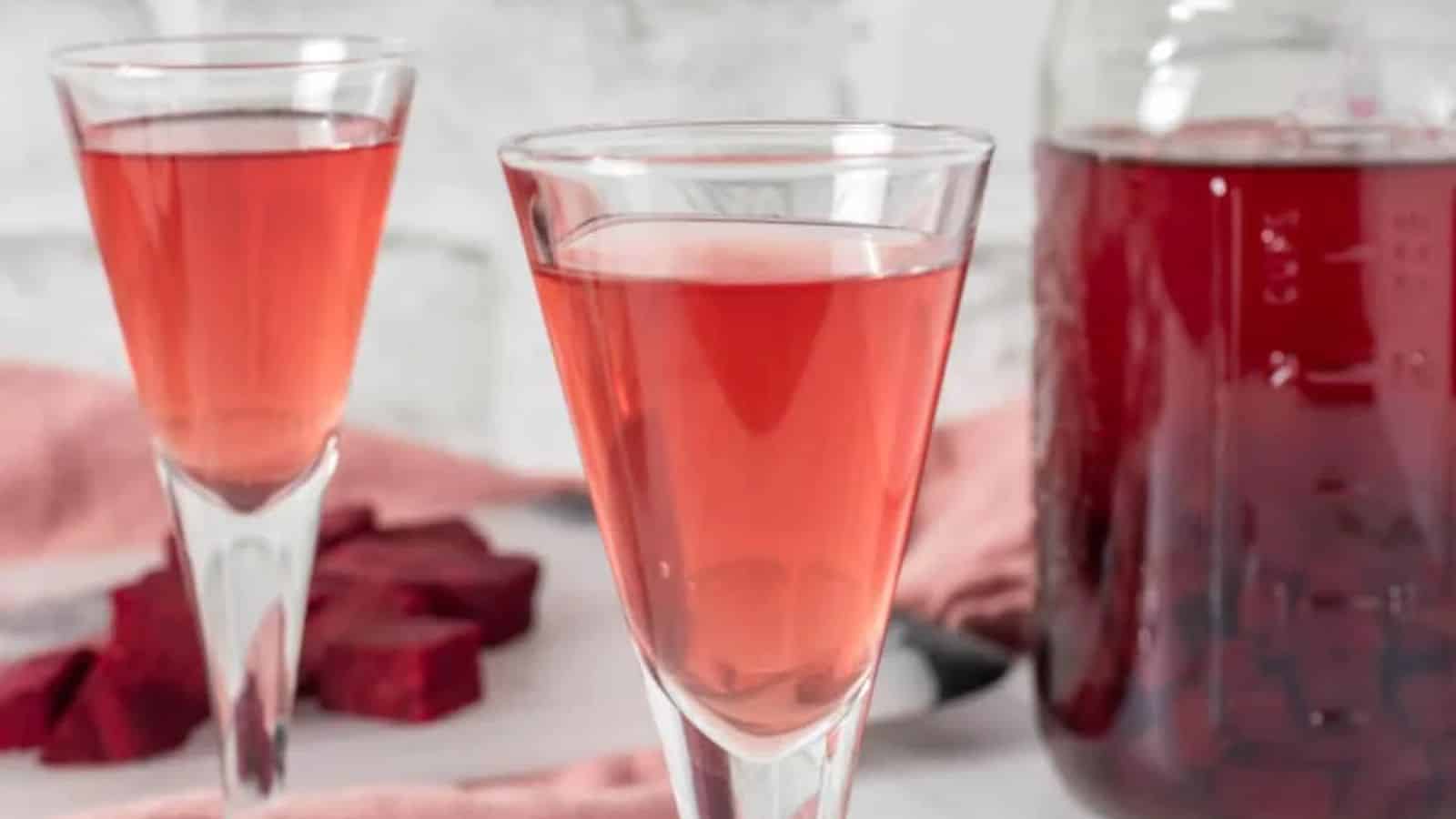 A close-up image of two glasses of beet kvass and a jar of it on the background.