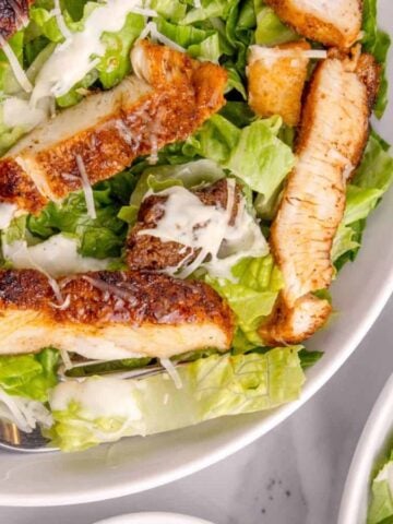 Top view of Chicken Caesar Salad bowls next to a cup of shredded cheese.