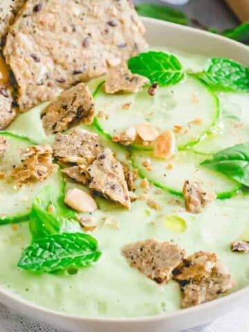 A bowl of Cucumber Gazpacho topped with slices of cucumber, some basil, and mint leaves.