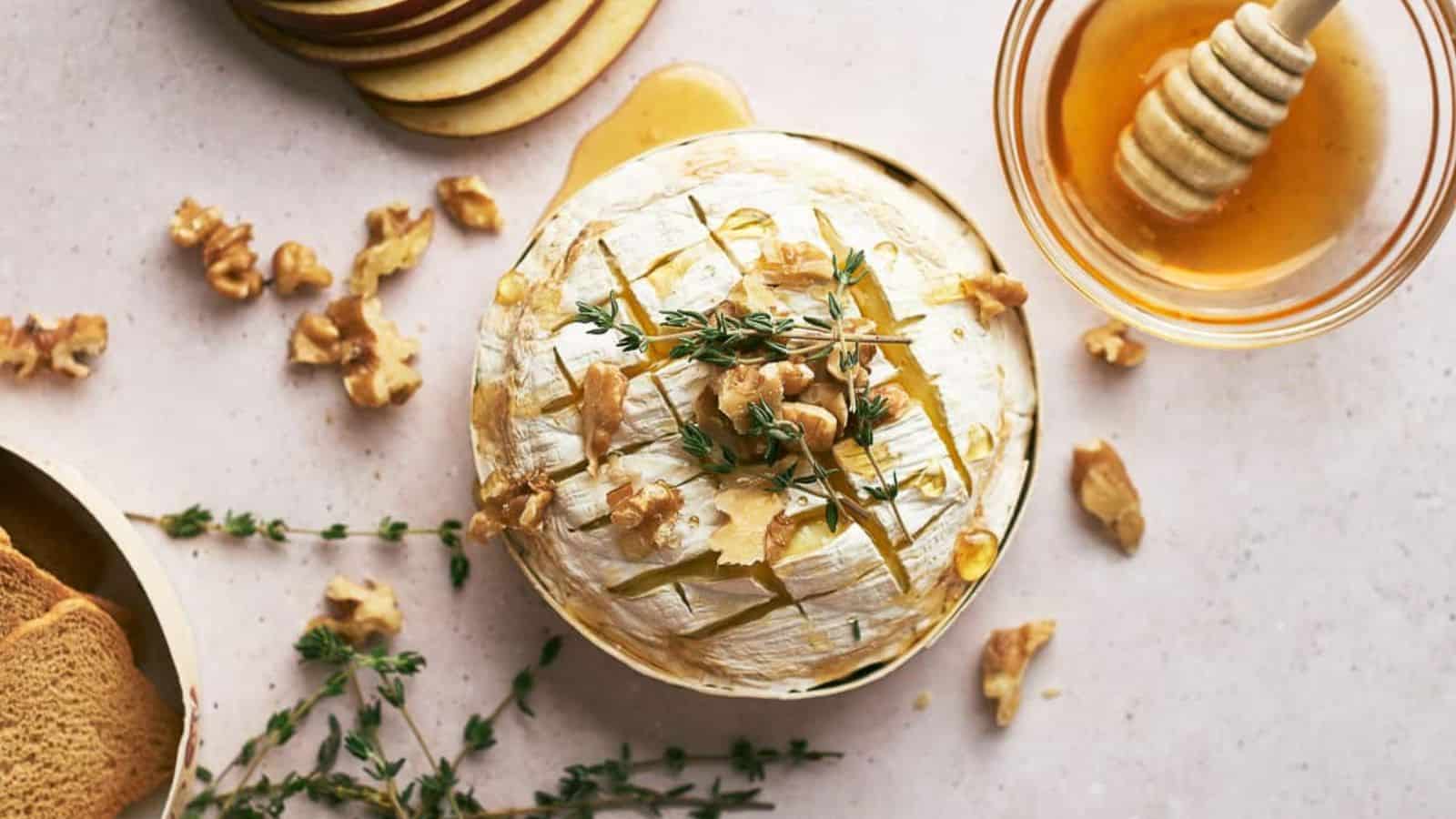 An overview of a Baked Brie, drizzle with honey, scatter with walnuts and pecans, and garnish with fresh thyme.