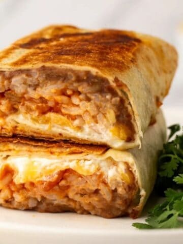 A close up image of cheesy bean and rice burrito on a plate.