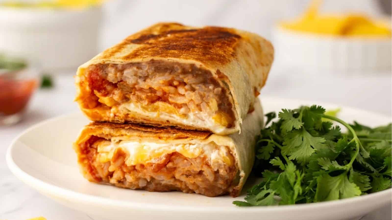A close up image of cheesy bean and rice burrito on a plate.