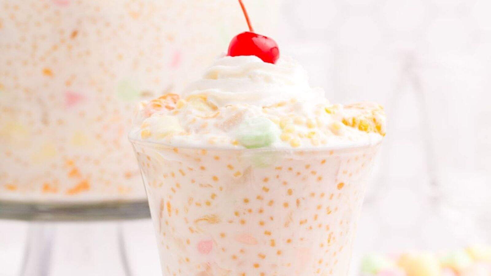 An image of Frog Eye Salad on a glass cup topped with cherry.