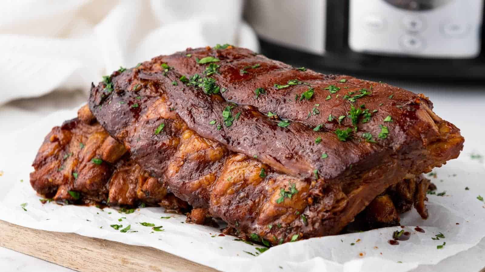 A cooked rack of baby back ribs garnished with chopped herbs sits on parchment paper.