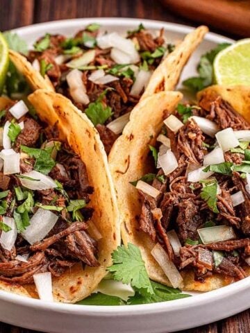 Three Slow Cooker Mexican Shredded Beef on a plate with slices of limes.