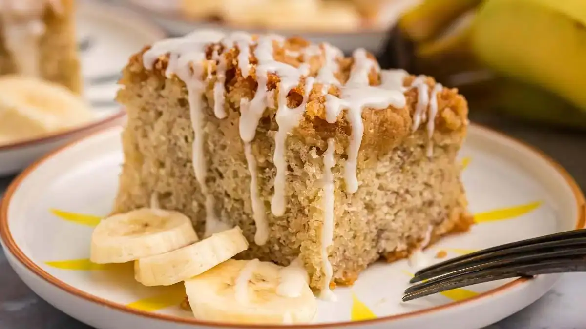 A serving of Banana Bread Crumb Cake on a plate with three slices of fresh bananas.
