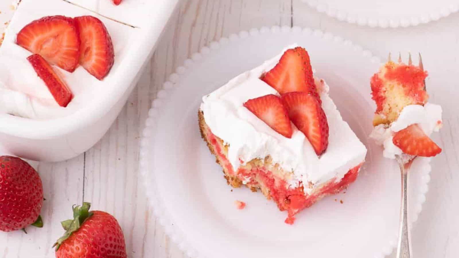 A slice of Strawberry Jello Cake on a white plate with a fork.