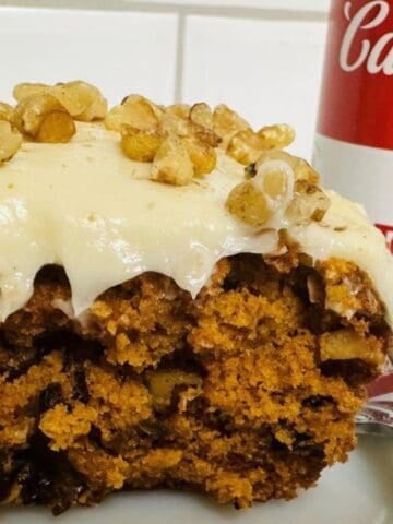 A piece of cake is sitting on a plate next to a can of soup.