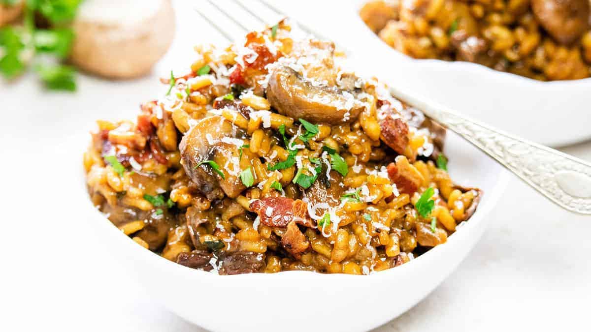 Mushroom and Bacon Risotto in a white bowl scattered with fresh herbs.