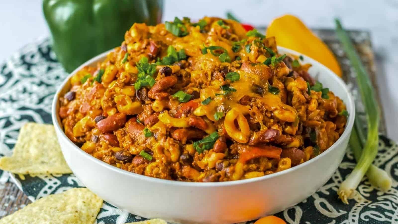 Cheese covered slow cooker chili mac in the crock pot with a wooden spoon.