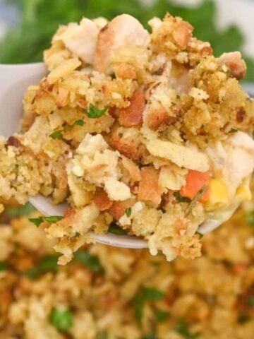 A spoon lifting chicken and stuffing casserole from a cast iron skillet, with a striped towel in the background.