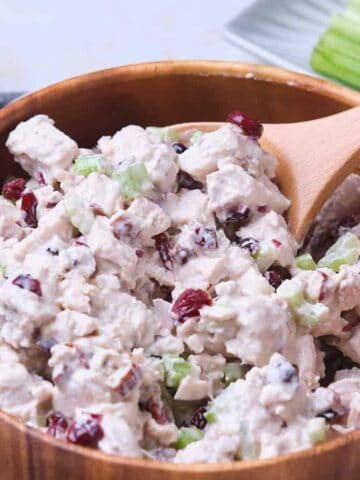 A wooden bowl filled with cranberry chicken salad with a wooden spoon.