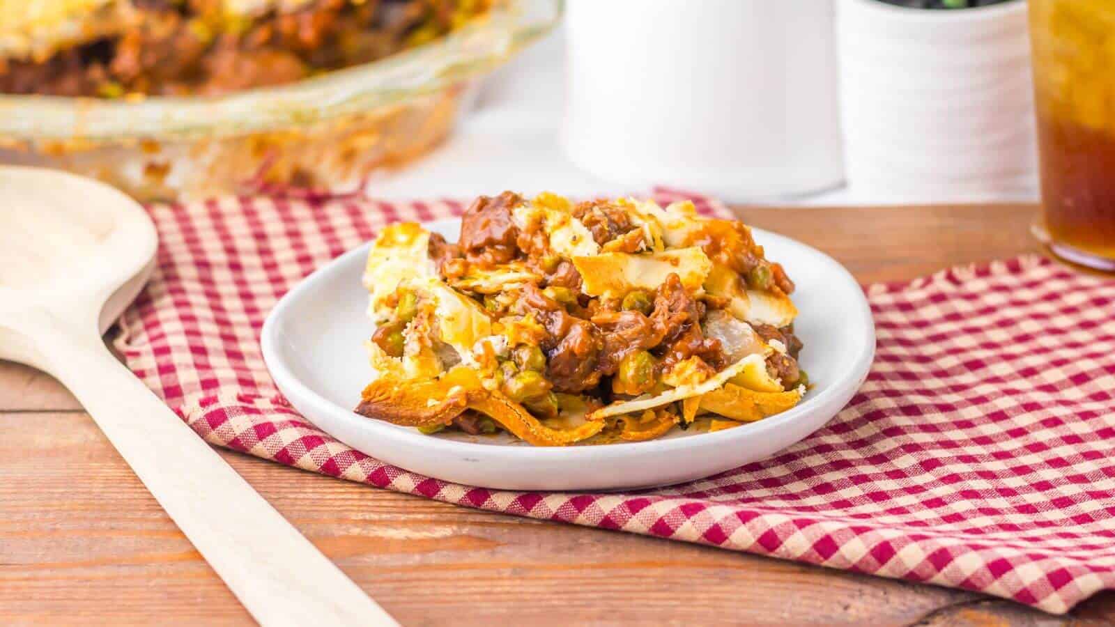 A plate of beef pot pie on a red and white checked cloth, next to a wooden spoon.