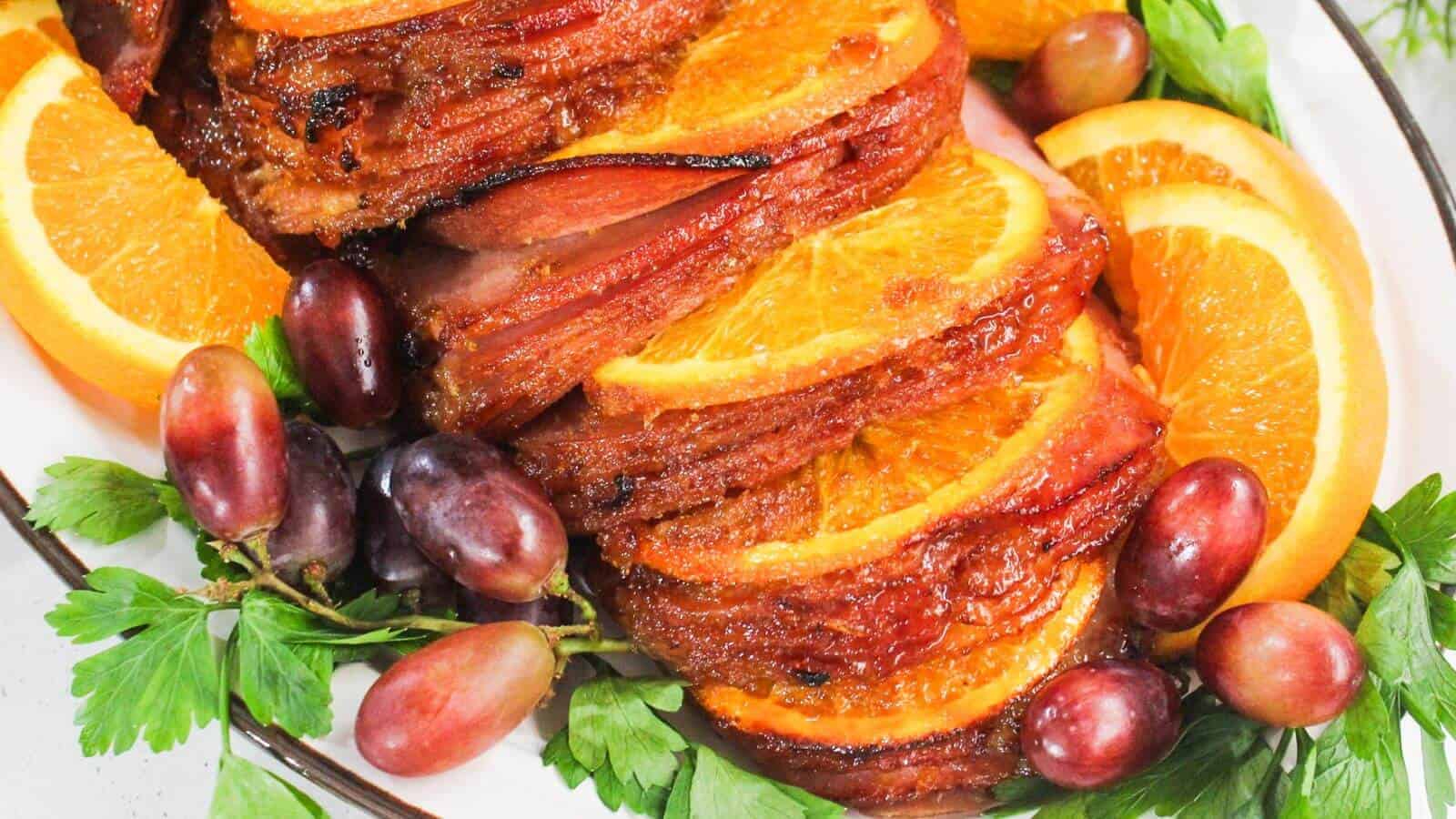 Sliced ham with orange slices and grapes, garnished with parsley on a platter.