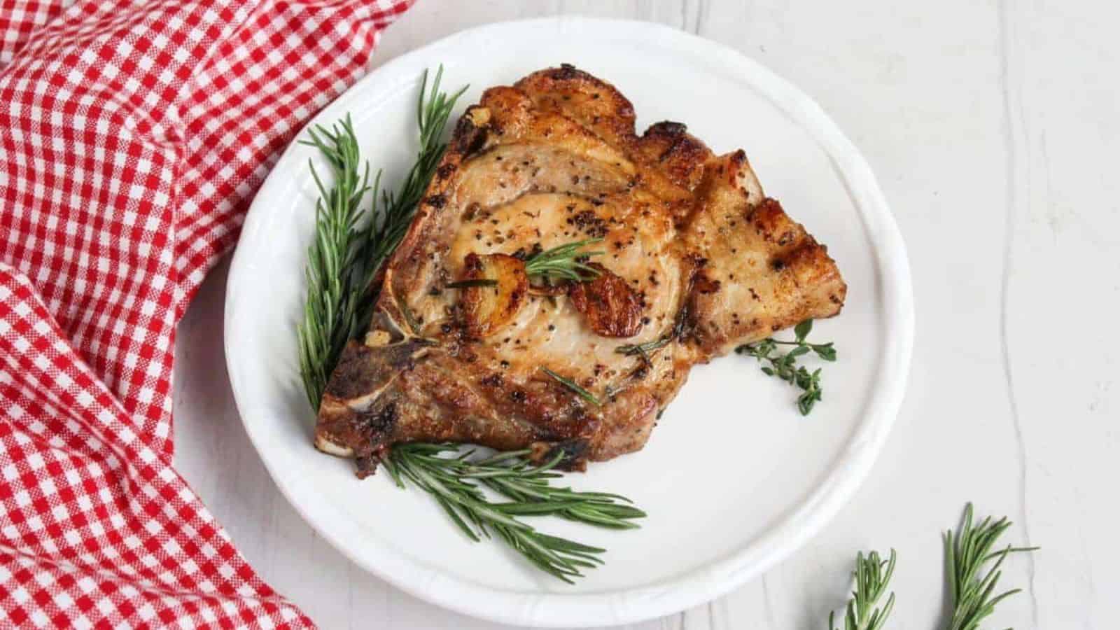 Pork chops on a plate with rosemary sprigs.