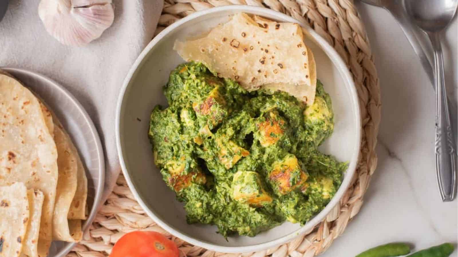 An overhead image of high protein palak paneer in a bowl with naan on the side.